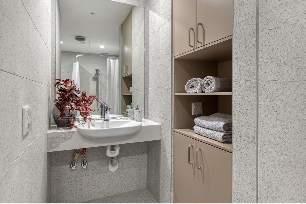 Vanity area inside the accessible bathroom, showing a wall-mounted basin with knee clearance, mirror and integrated storage cabinetry.