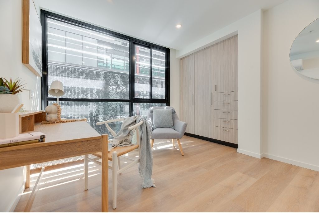 Second bedroom inside the Essendon SDA apartment, showing timber-look flooring, built-in wardrobe, desk area and large windows.
