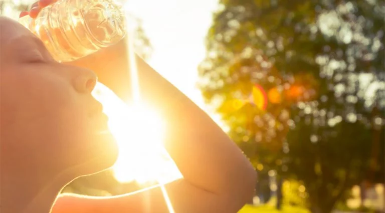 Women holding a water bottle to her head in the bright sun