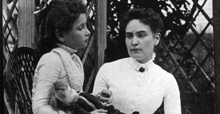 Helen Keller holding a doll while sitting with her Teacher, Anne Sullivan
