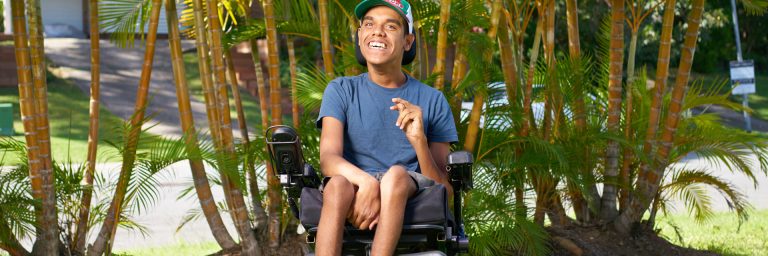 Man who uses a wheelchair outside in front of some trees