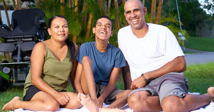 Man with a disability sitting outside on a picnic rug with his family