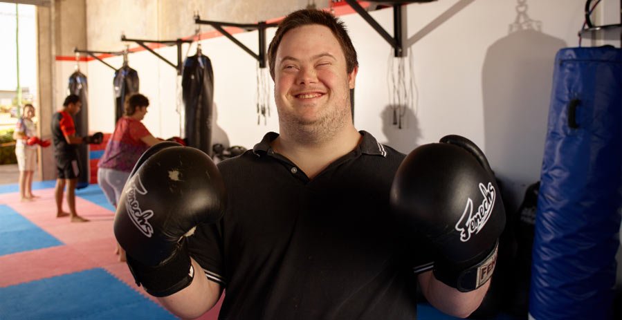 Man with Down syndrome wearing boxing gloves and smiling in a disability service