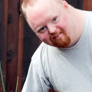 Man with Down syndrome standing in front of a wooden structure