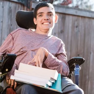 Man with a disability using a wheelchair outside with a stack of books on his lap