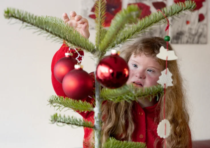 Girl with Down Syndrome adding a round bauble to a Christmas tree.
