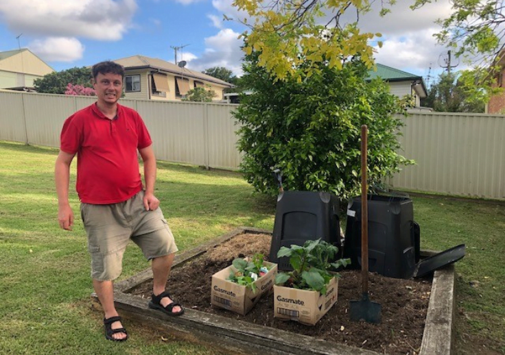 Andrew wearing a red shirt and smiling as he poses with his garden.
