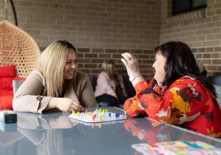 A customer and a support worker laughing together while playing a board game