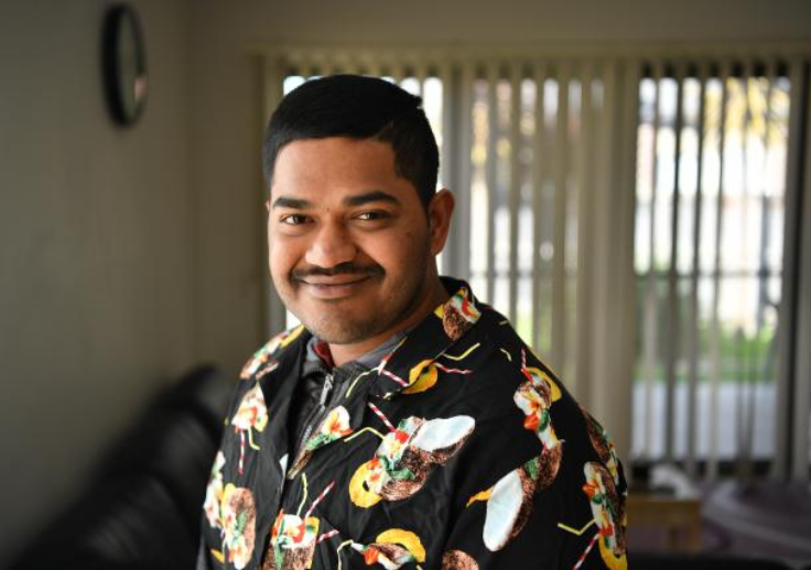 Aruma customer Ajish smiling in his home and wearing a brightly coloured shirt.