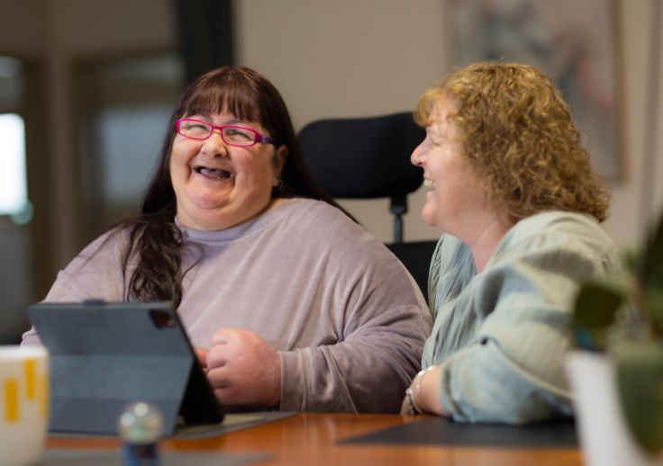 A customer and a support worker at one of our homes. They are both smiling and using an ipad